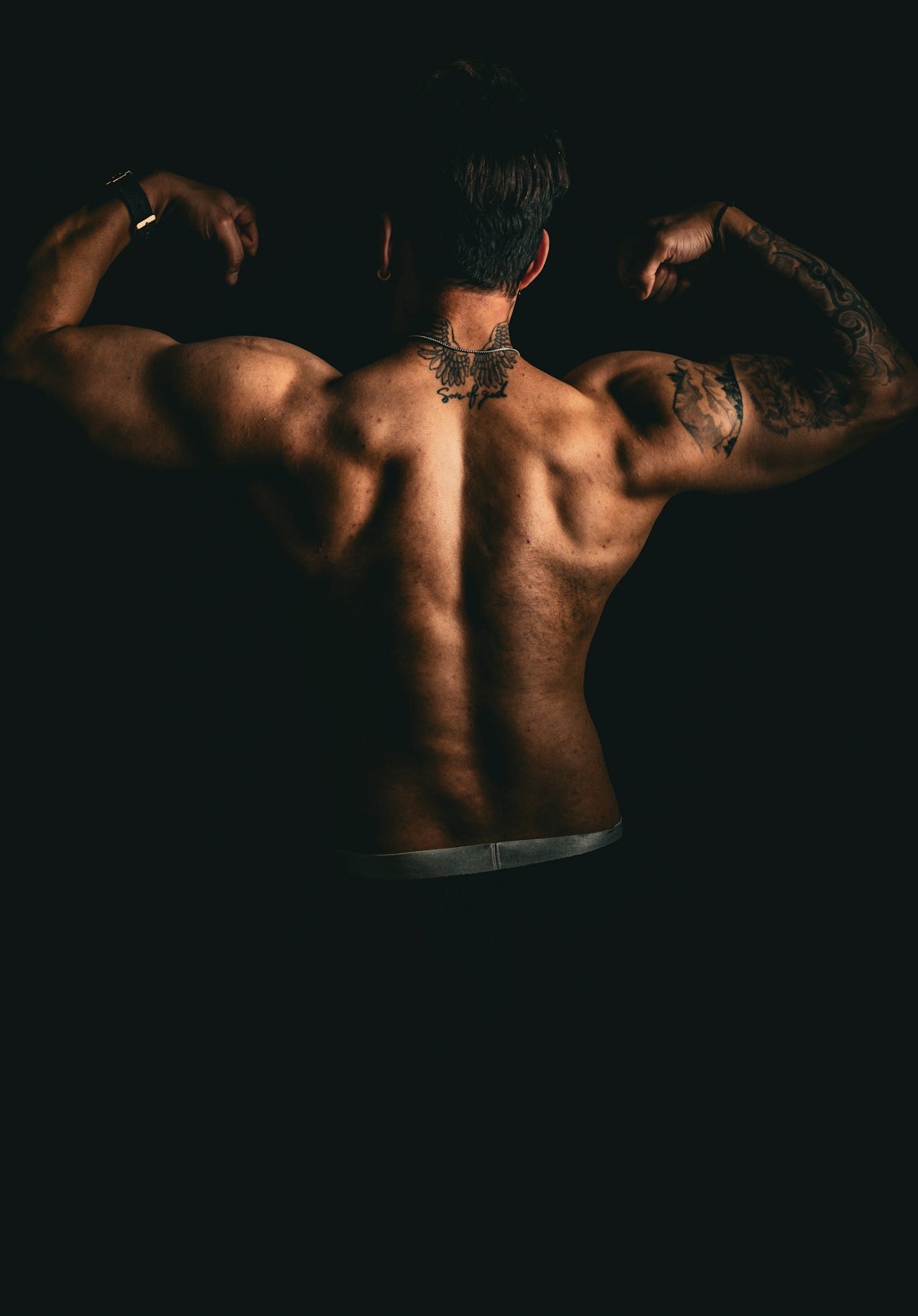 Muscular man flexing his back muscles with tattoos.